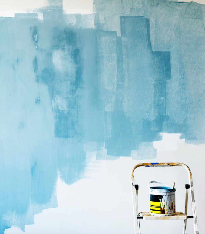 Mur en cours de mise en peinture avec aplats bleus de test, seau de peinture et escabeau avant application de la finition